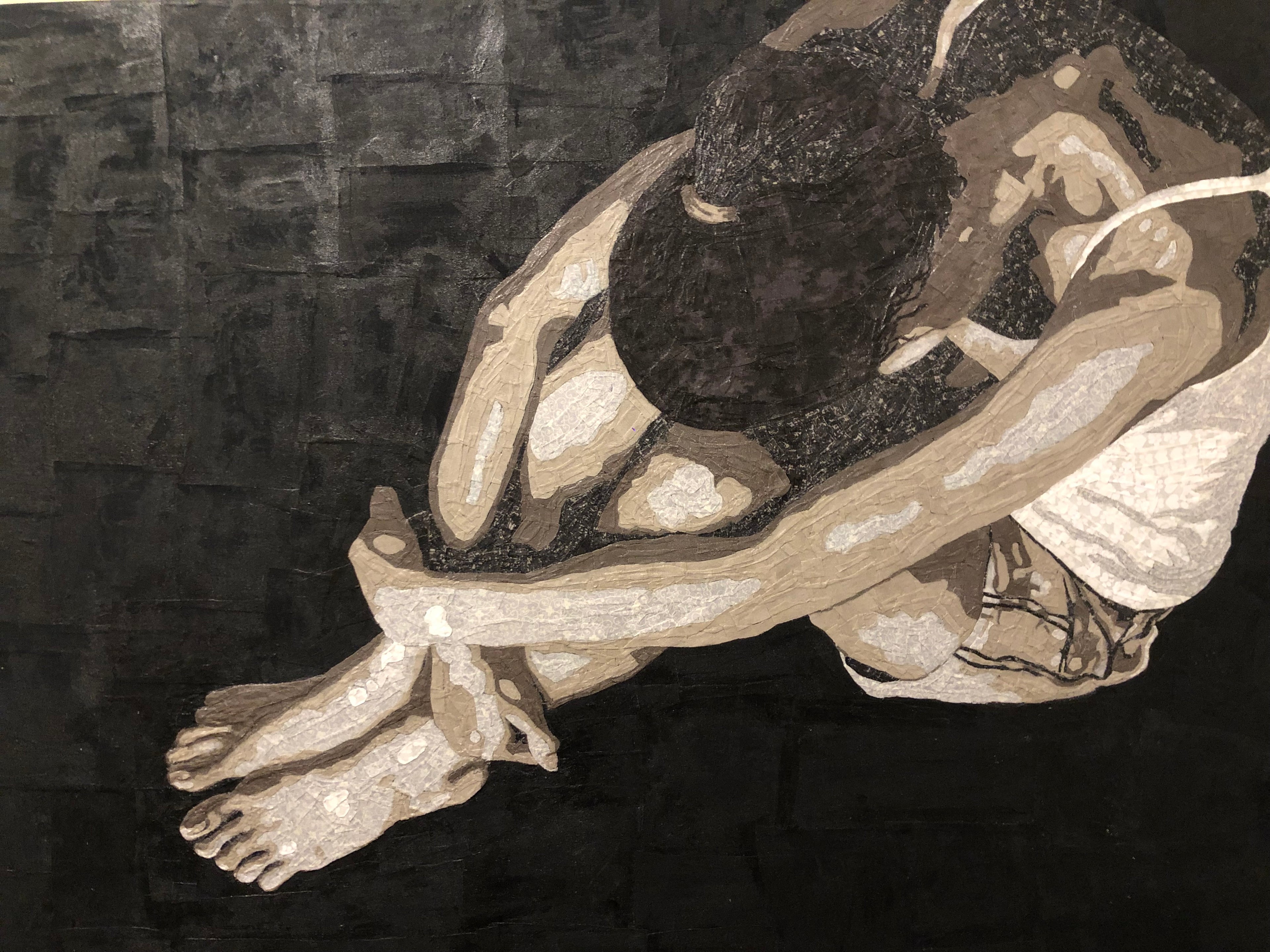 this is a textile art piece that shows a woman with her head in her lap, lamenting over her life. She's surrounded by a black background